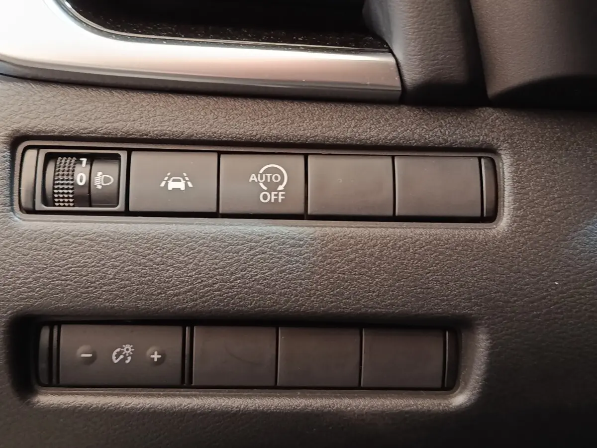 Gros plan sur les boutons de commande du tableau de bord noir du Nissan Qashqai 1.3 MHEV gris foncé, avec régulateur de luminosité et aides à la conduite.