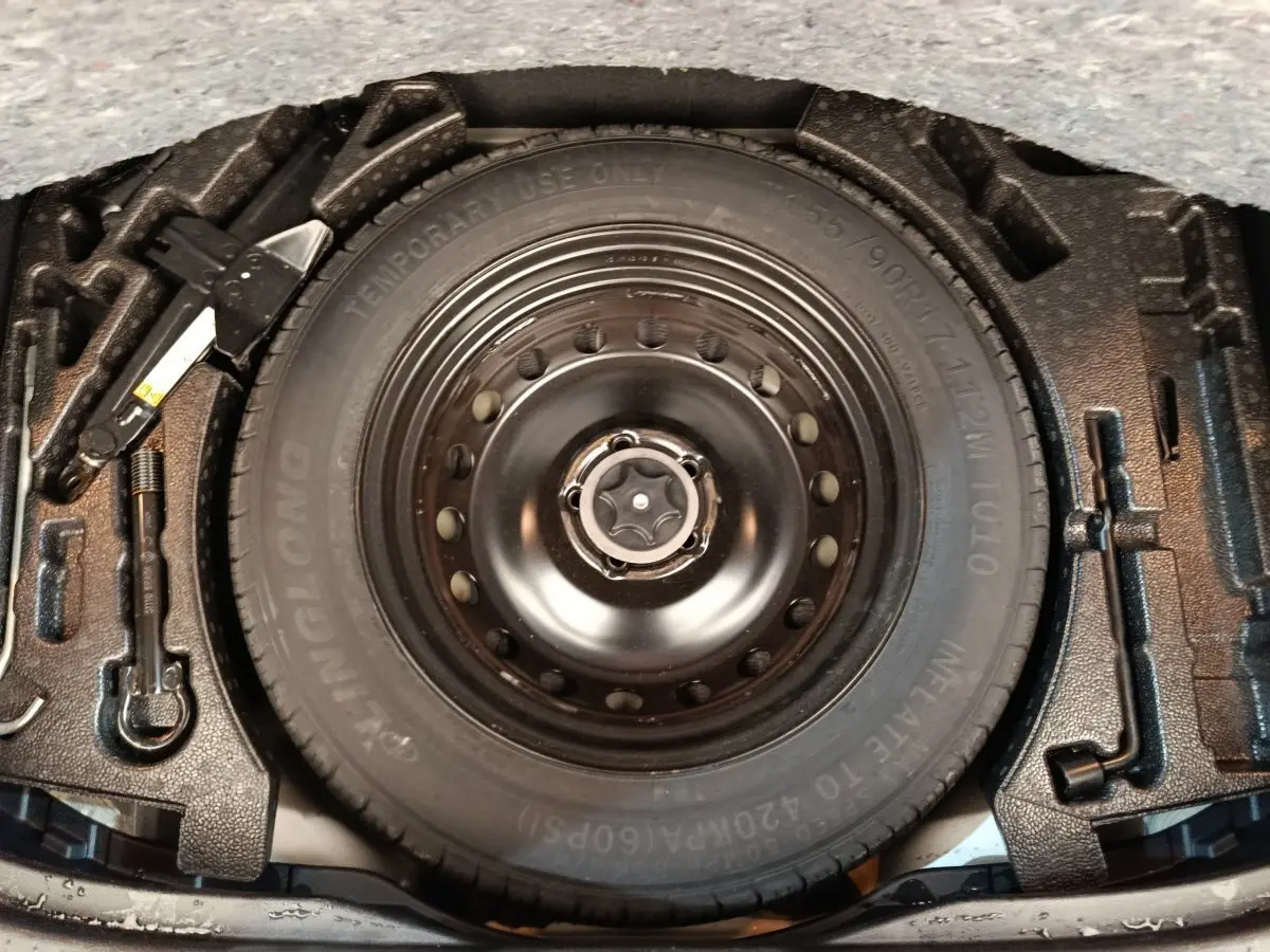 Vue rapprochée de la roue de secours noire et des outils de changement de pneu dans le coffre d’un Nissan Qashqai gris foncé.