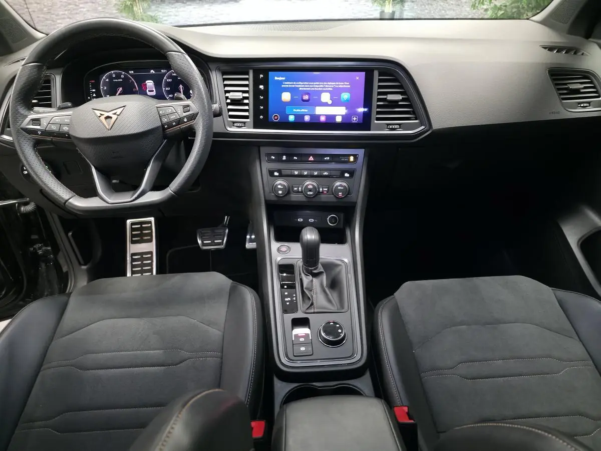 Vue intérieure centrée du tableau de bord et console centrale du CUPRA Ateca 2024 avec volant sport et sièges en suédine noir.