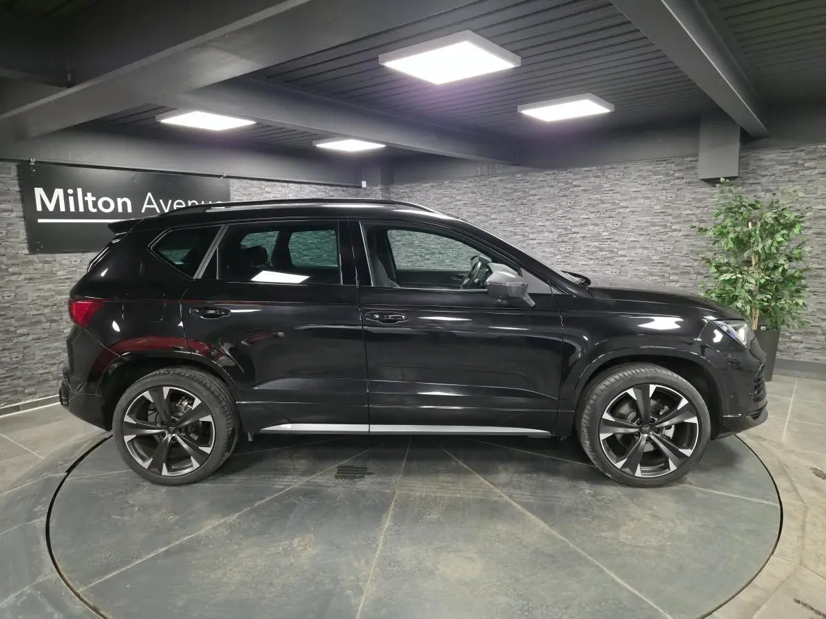 Vue de profil côté gauche d’un CUPRA Ateca noir brillant avec jantes alliage 19 pouces dans un showroom intérieur.