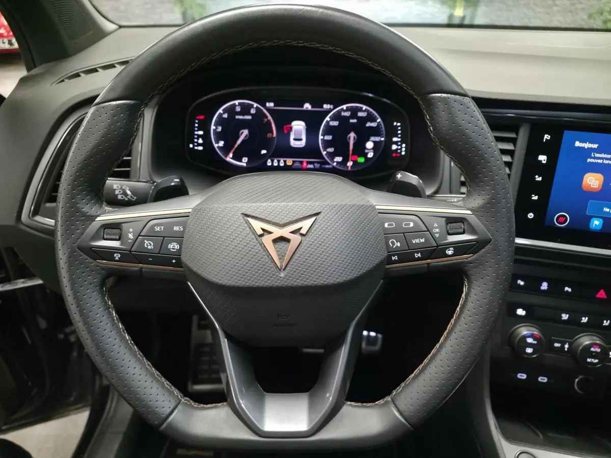 Vue rapprochée du volant sport en cuir perforé noir avec logo CUPRA cuivre et tableau de bord numérique.
