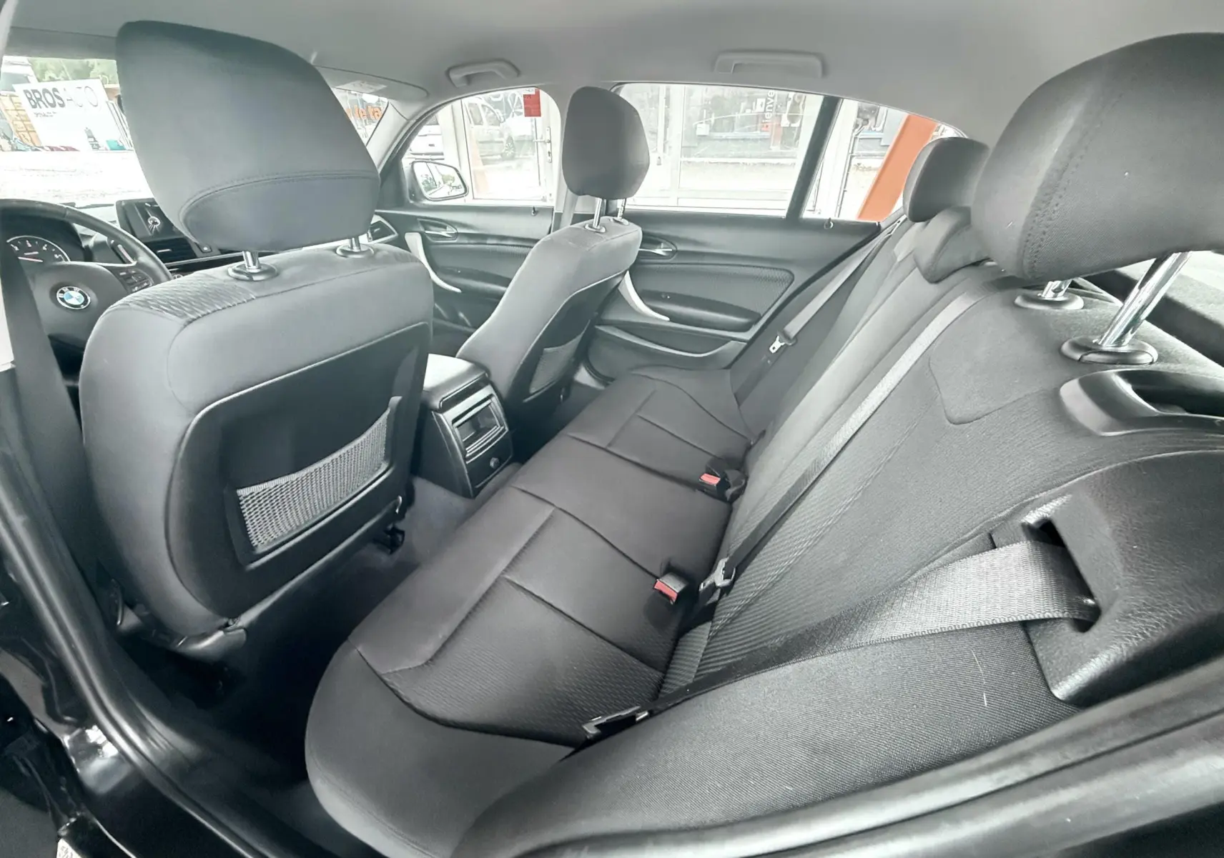 Vue intérieure arrière de la BMW Série 1 noire, montrant les sièges arrière en tissu noir et les dossiers des sièges avant.