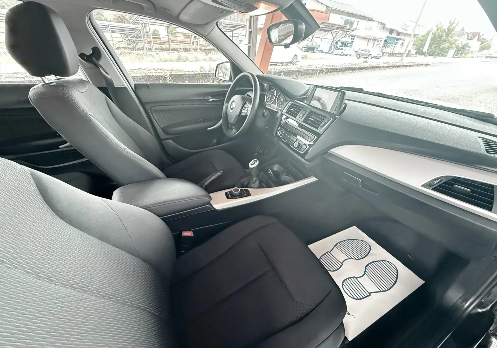 Vue intérieure côté passager avant de la BMW Série 1 noire, montrant sièges tissu noirs et tableau de bord moderne.