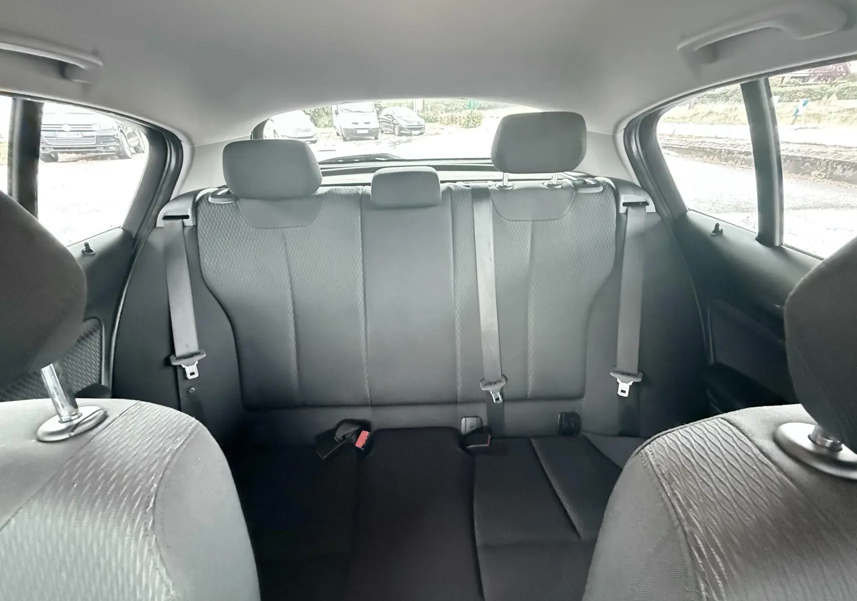 Vue intérieure arrière de la BMW Série 1 noire, montrant les sièges arrière en tissu noir avec ceintures de sécurité.