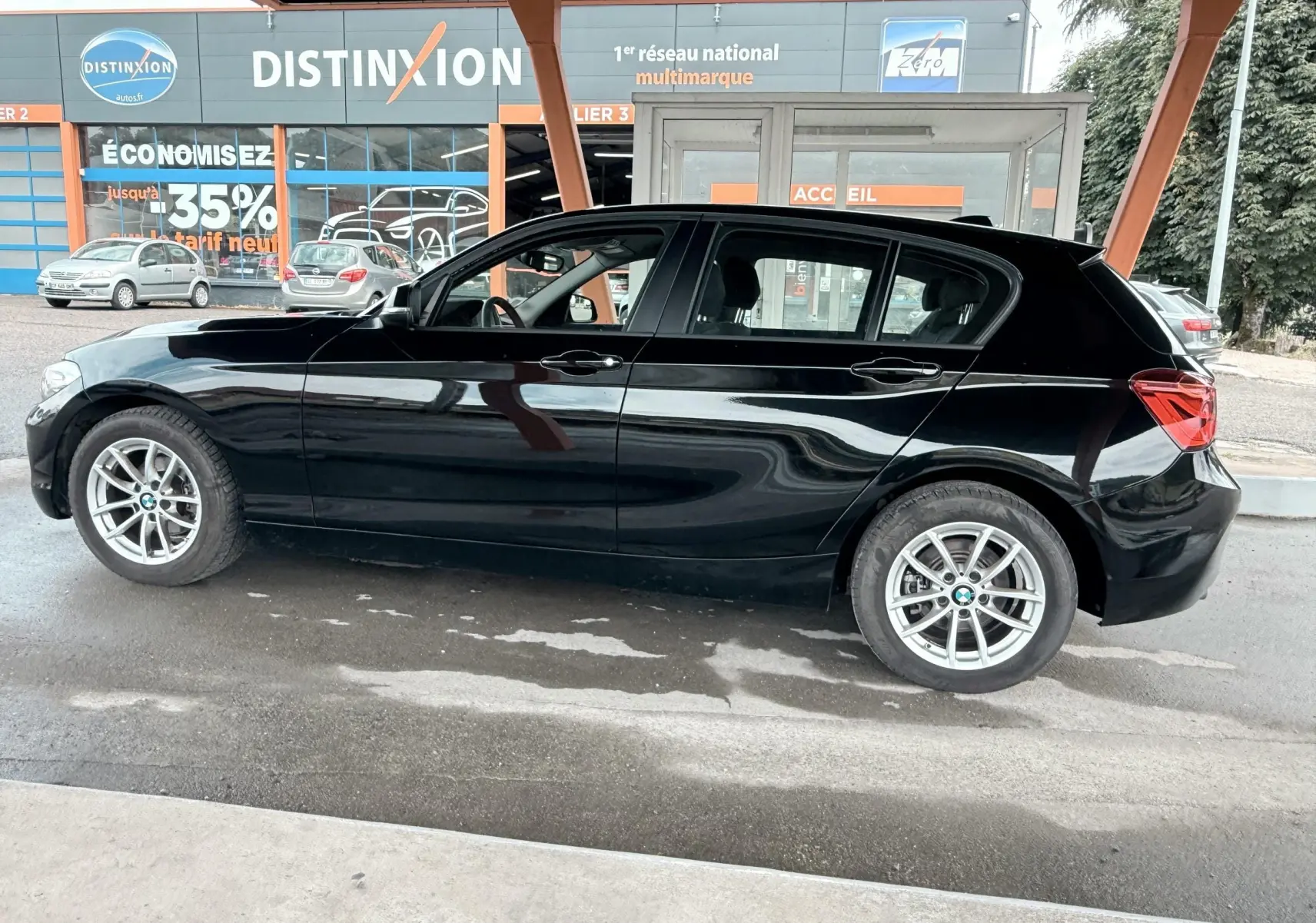 BMW Série 1 noire vue de profil côté gauche, avec jantes alliage et carrosserie lisse sous un abri.