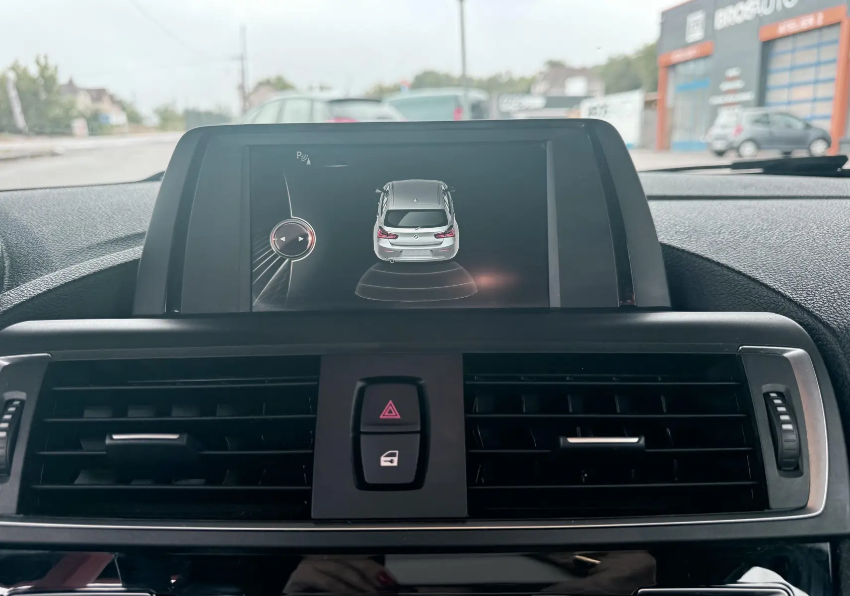 Vue intérieure centrée sur l'écran multimédia affichant l'aide au stationnement de la BMW Série 1 noire de 2016.