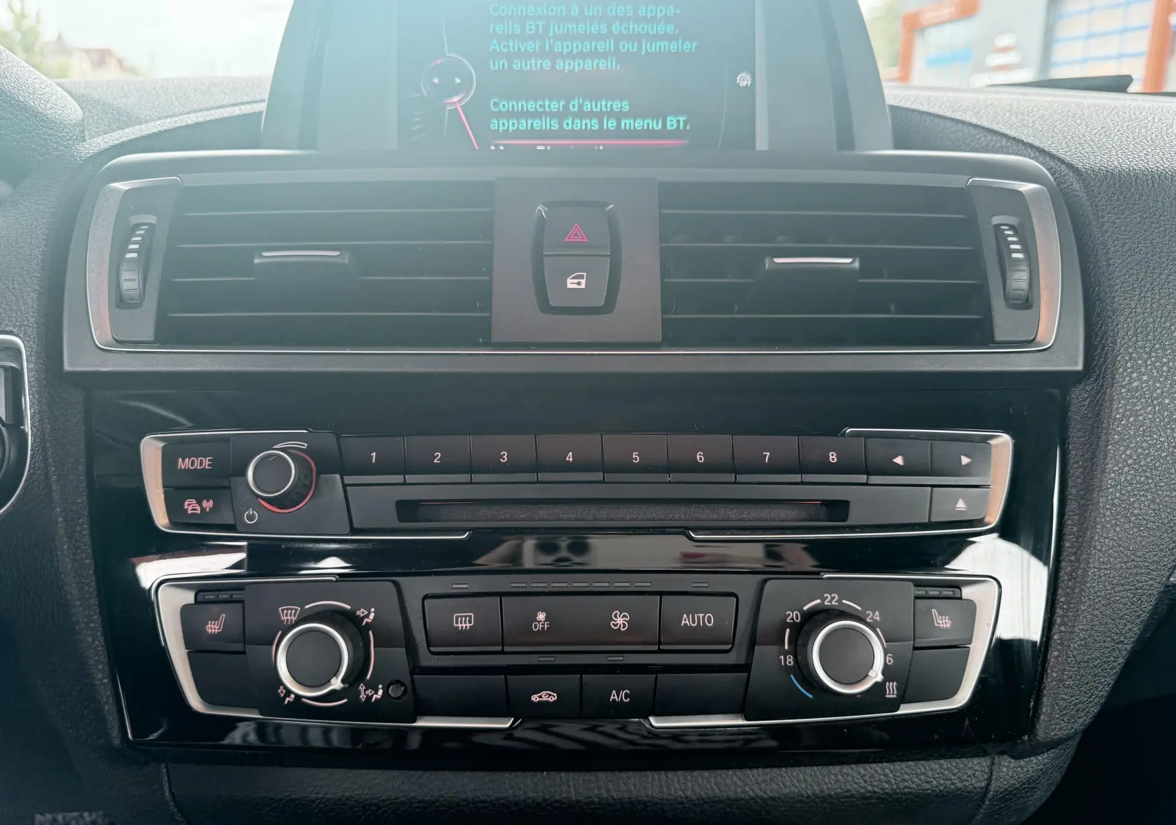 Vue rapprochée du tableau de bord central de la BMW Série 1 noire, montrant la console multimédia et les commandes de climatisation.
