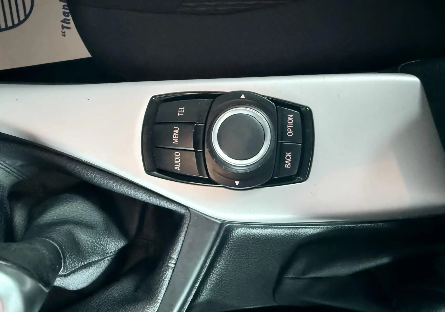 Gros plan sur la molette de commande multimédia et levier de vitesse en cuir noir de la BMW Série 1 2016.