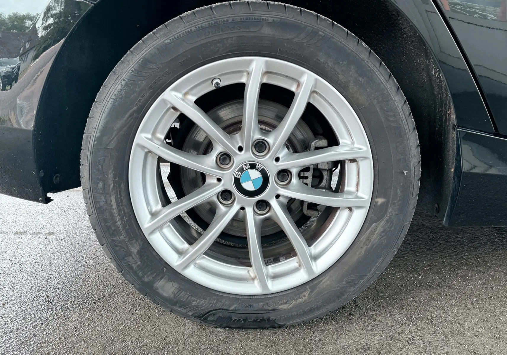 Gros plan sur la roue avant droite d’une BMW Série 1 noire, mettant en valeur la jante alliage argentée et le logo BMW central.