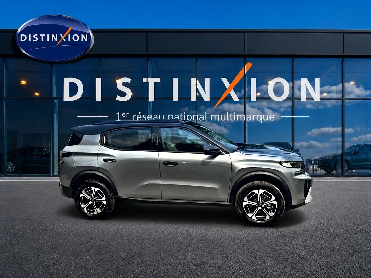 Vue de profil côté gauche d'un Citroën C3 Aircross gris mercury devant une vitrine Distinxion.