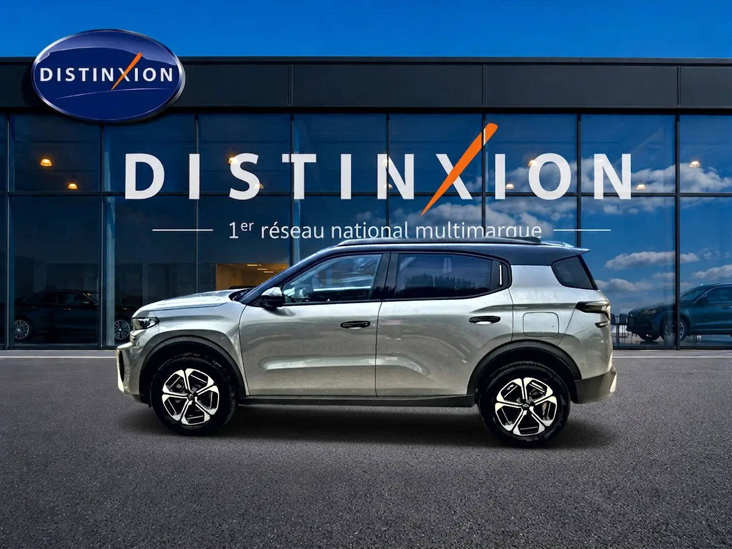 Vue latérale gauche d'un Citroën C3 Aircross gris mercury 2026 avec jantes alliage et toit noir devant un showroom Distinxion.
