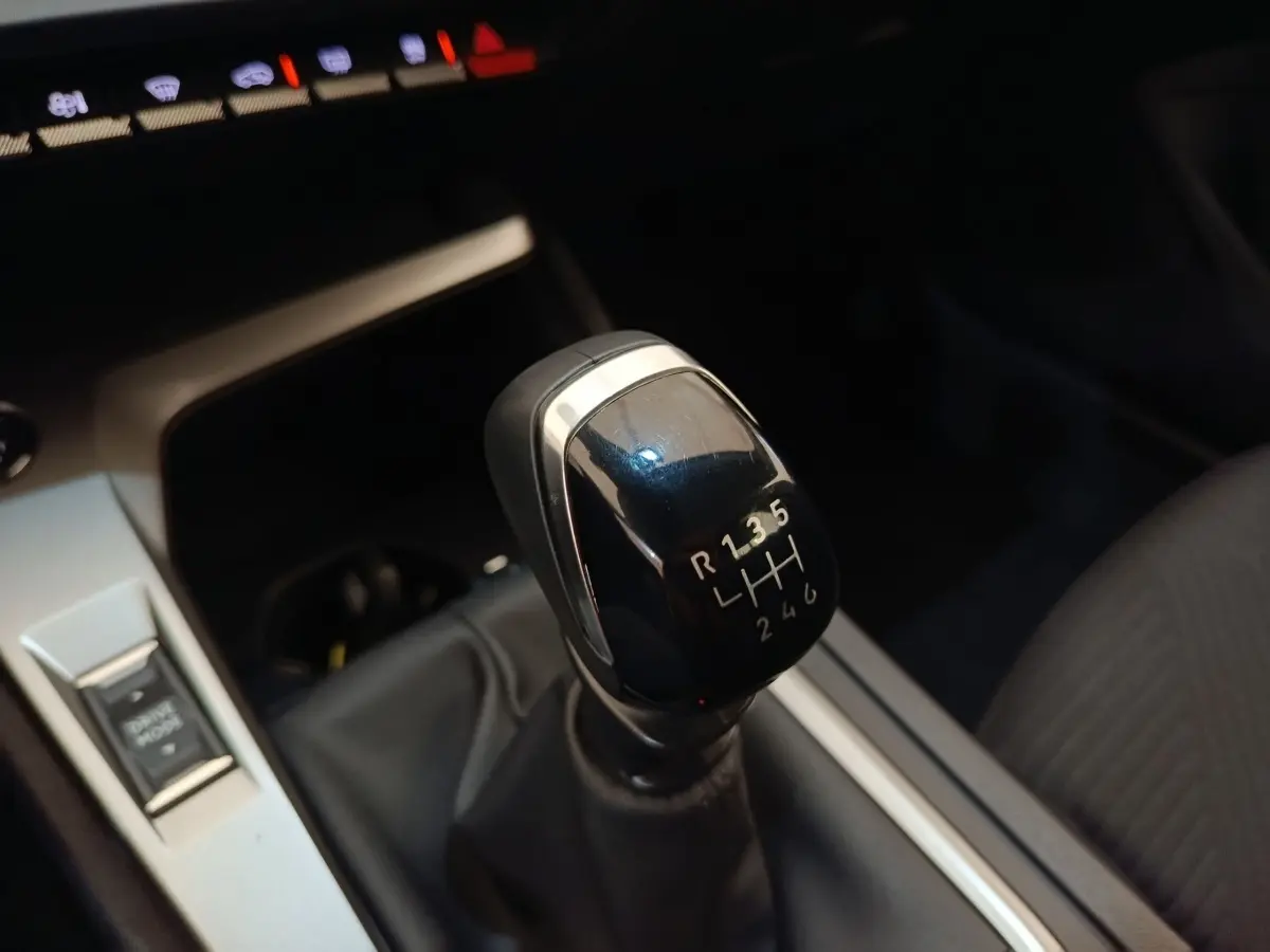 Gros plan sur le levier de vitesses manuel noir de la Peugeot 308 2024, intérieur avec console argentée et siège tissu gris.