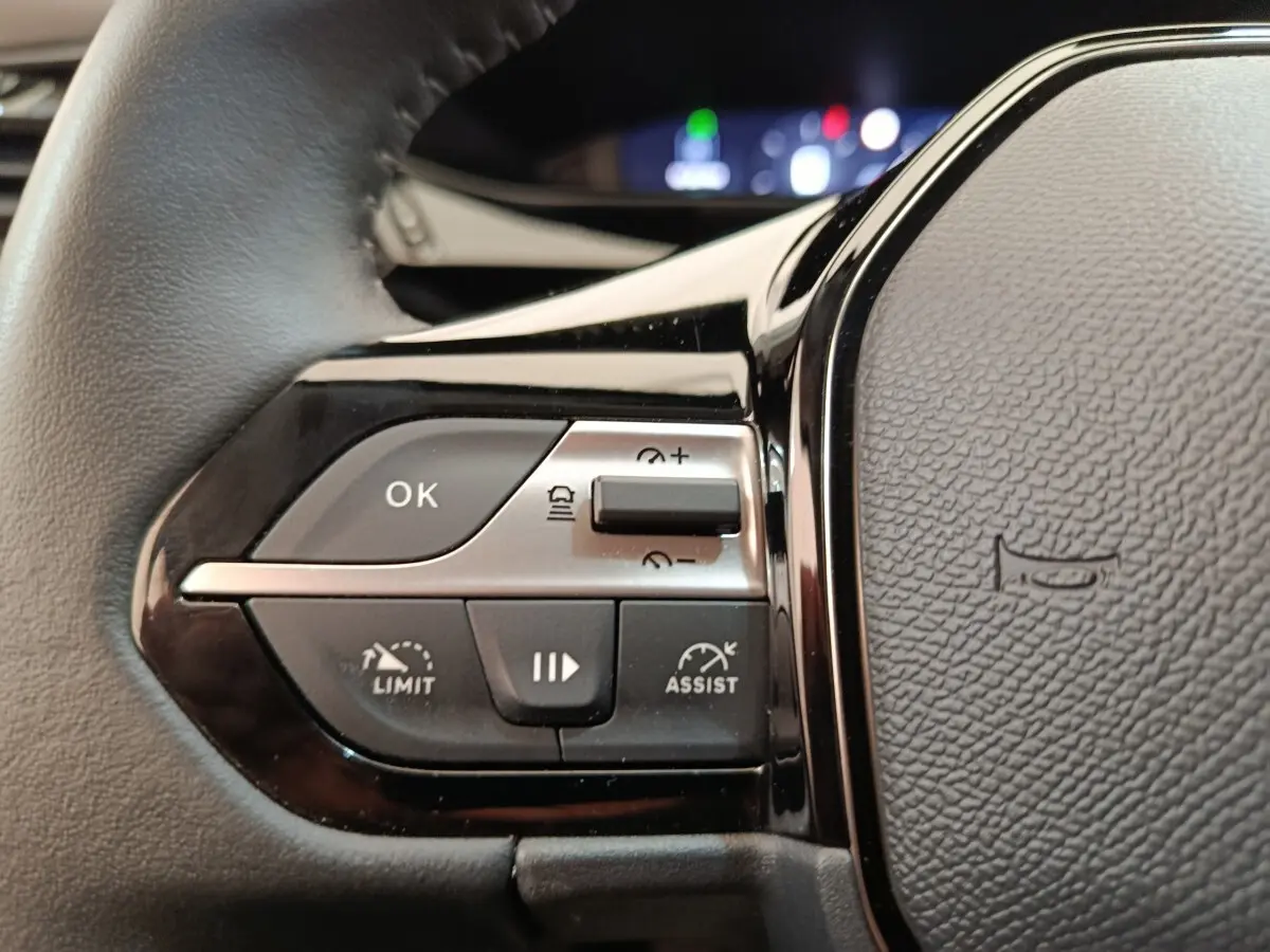 Gros plan sur les commandes gauche du volant cuir noir d’une Peugeot 308 blanche, avec boutons de régulateur et assistances.