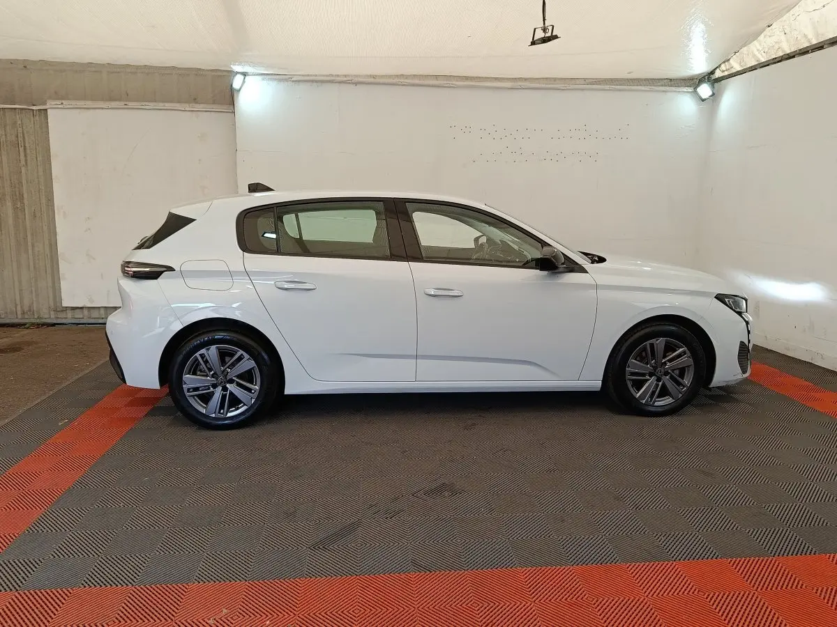 Peugeot 308 blanche vue de profil côté gauche dans un garage, avec jantes alliage et feux arrière LED distinctifs.