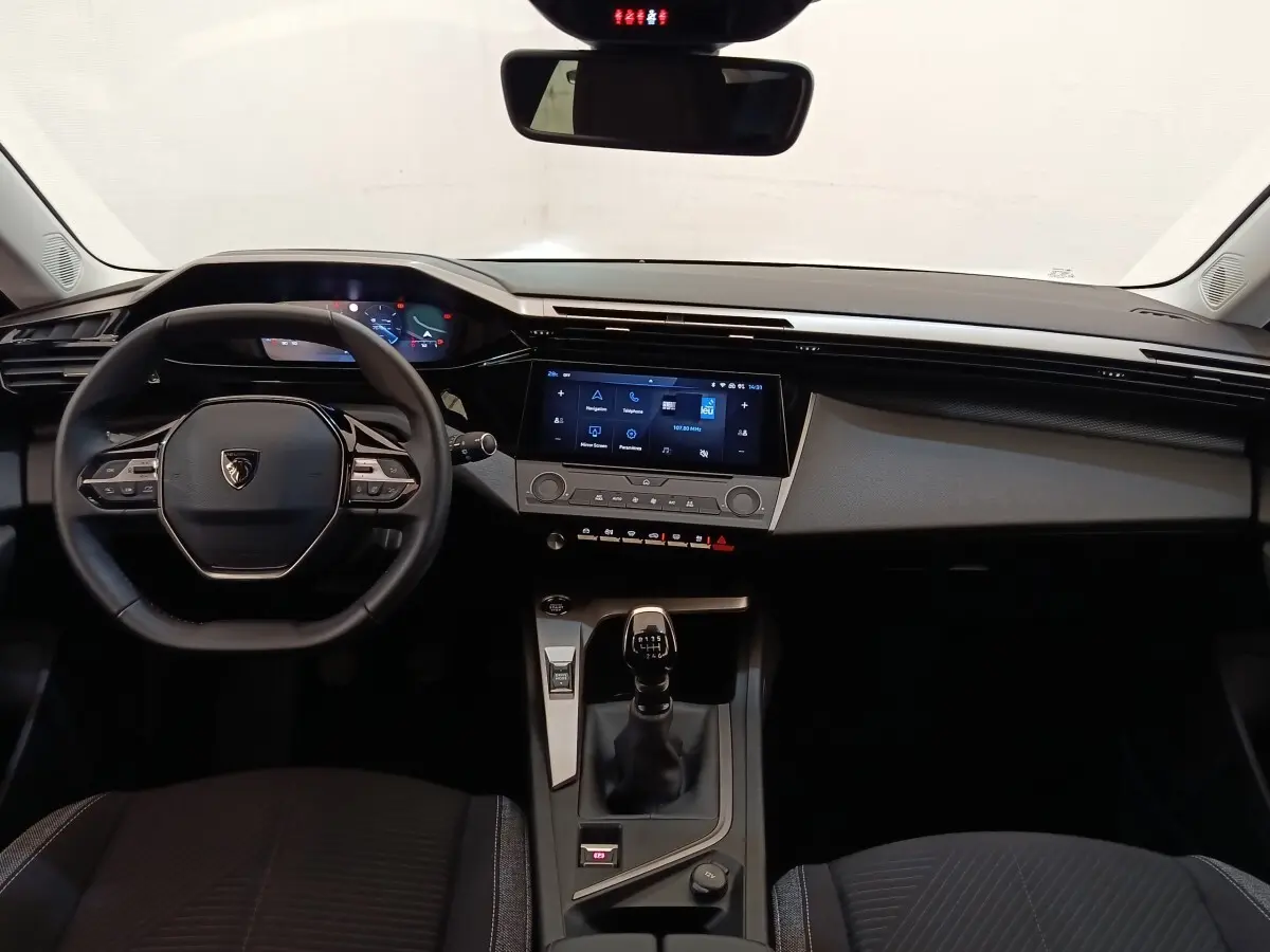 Vue intérieure frontale du poste de conduite de la Peugeot 308 blanche, avec volant cuir et écran tactile central.
