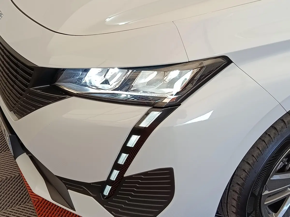 Gros plan sur l'avant droit blanc d'une Peugeot 308 2024, mettant en valeur le phare LED et la calandre noire.