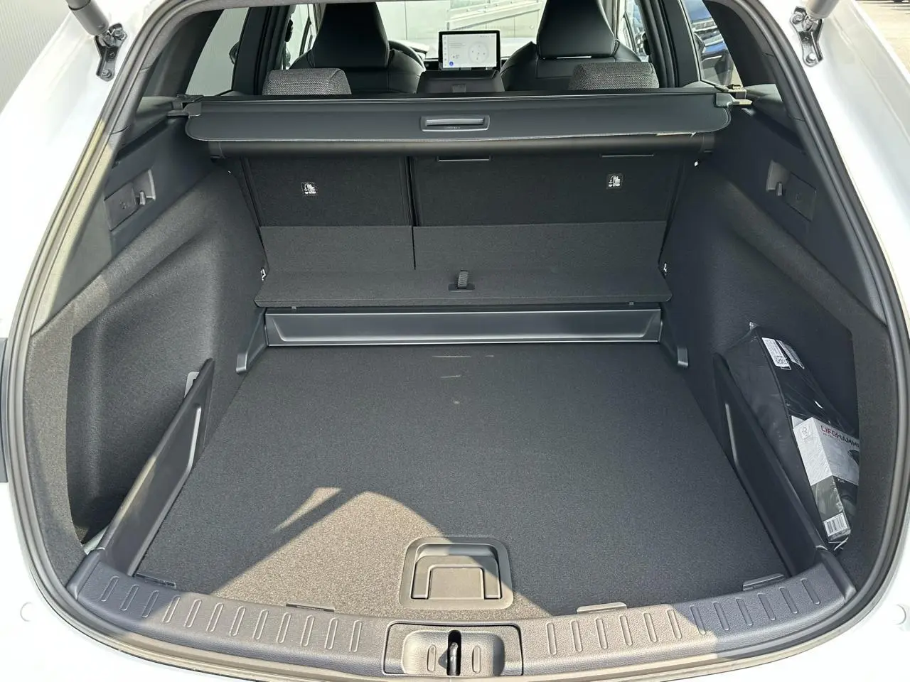 Coffre ouvert vu de l'arrière d'une Toyota Corolla Touring Sport 1.8 Hybrid blanc neige, intérieur noir spacieux.