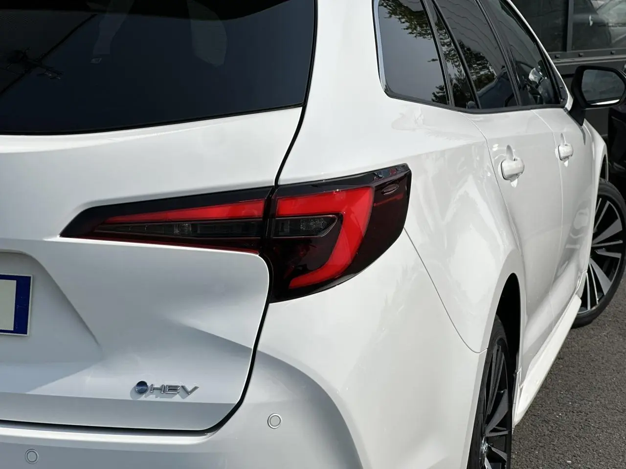 Vue 3/4 arrière droite d'une Toyota Corolla Touring Sport blanche Neige avec feux arrière LED et jantes alliage noires.
