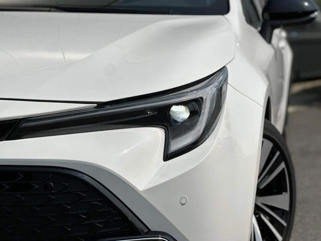 Gros plan sur le phare avant droit blanc neige de la Toyota Corolla Touring Sport 2025 avec jante alliage noire et grise.