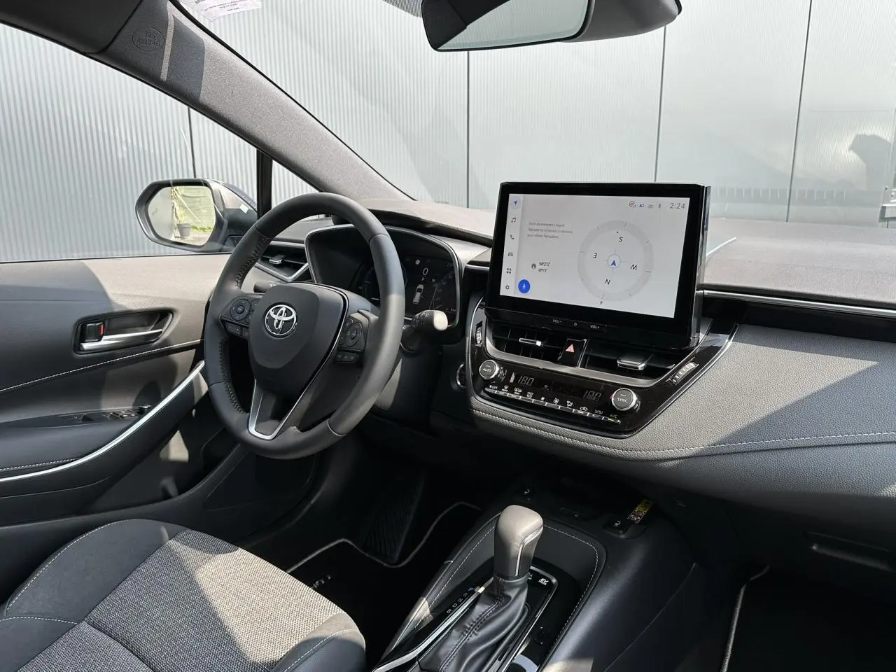 Intérieur de la Toyota Corolla Touring Sport 1.8 Hybrid 2025, vue côté conducteur, tableau de bord et écran tactile noir.