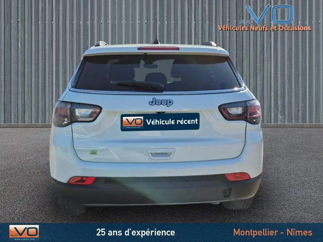 Vue arrière d'un Jeep Compass blanc 2023 avec feux arrière fumés et logo Jeep visible sur un fond neutre.