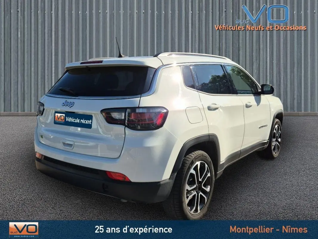 Vue 3/4 arrière droite d'un Jeep Compass blanc 2023 avec jantes 18 pouces et barres de toit visibles.