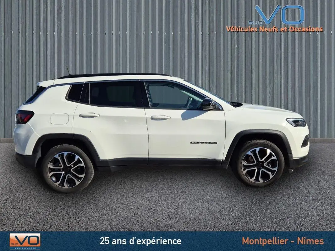 Vue de profil côté gauche d'un Jeep Compass blanc 2023 avec jantes 18 pouces et barres de toit noires.