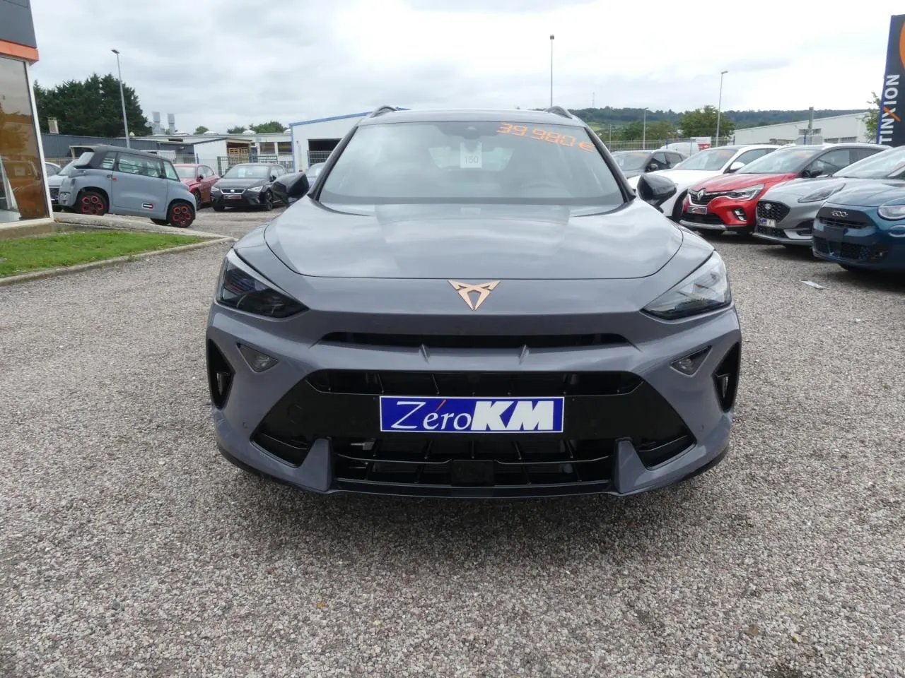 Vue frontale d'une CUPRA Formentor gris Graphène avec logo cuivré et calandre noire sur un parking.