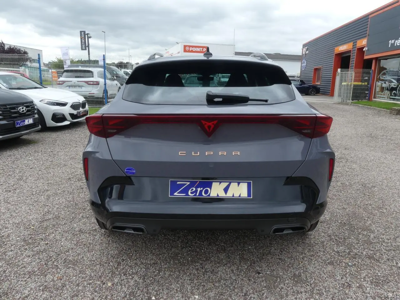 Vue arrière d'une CUPRA Formentor gris Graphene avec logo rouge et double sortie d'échappement noire sur parking.