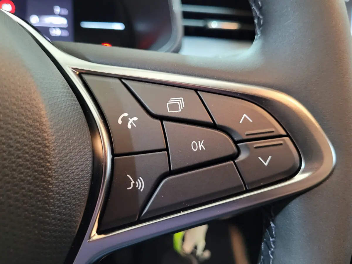 Gros plan sur les commandes multifonctions noires du volant côté gauche de la Renault Clio gris foncé Evolution Blue dCi 100 2025.