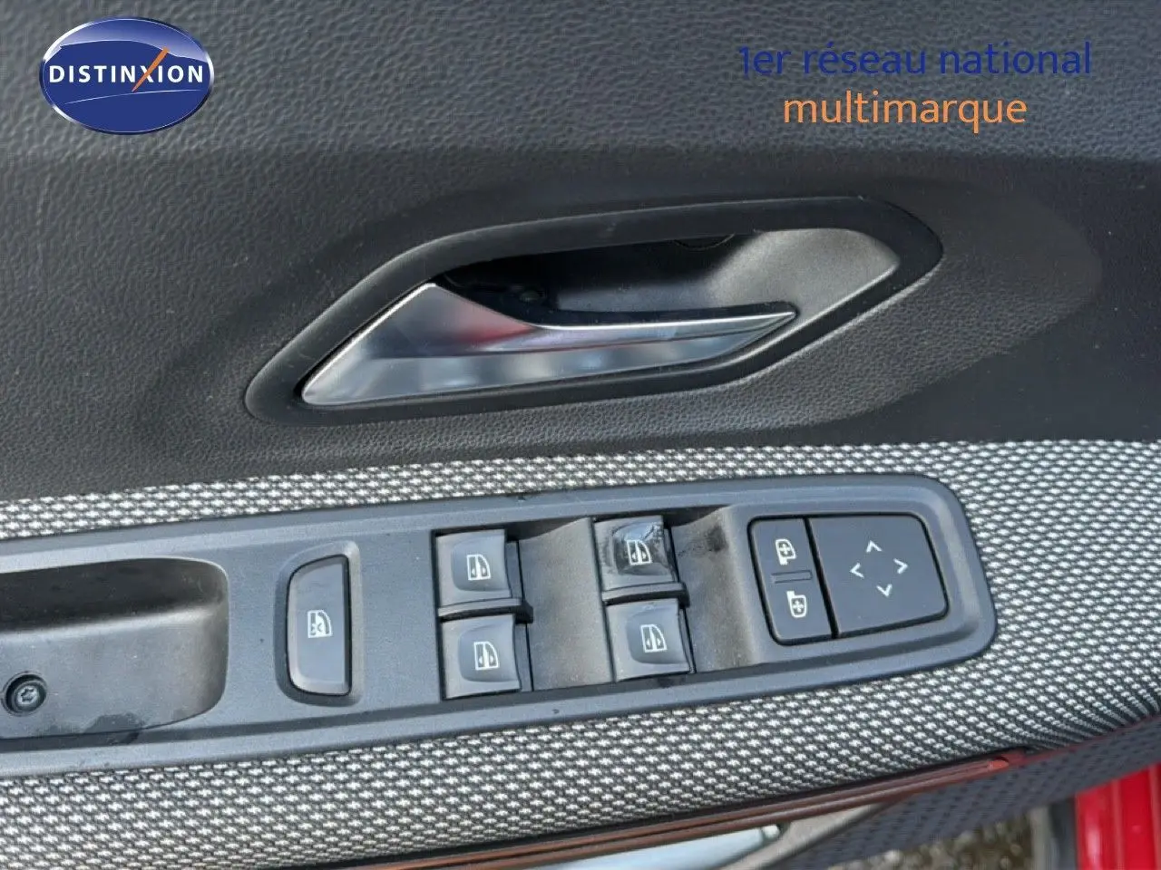 Gros plan sur la commande des vitres et la poignée intérieure côté conducteur d’une Dacia Sandero Stepway rouge fusion.