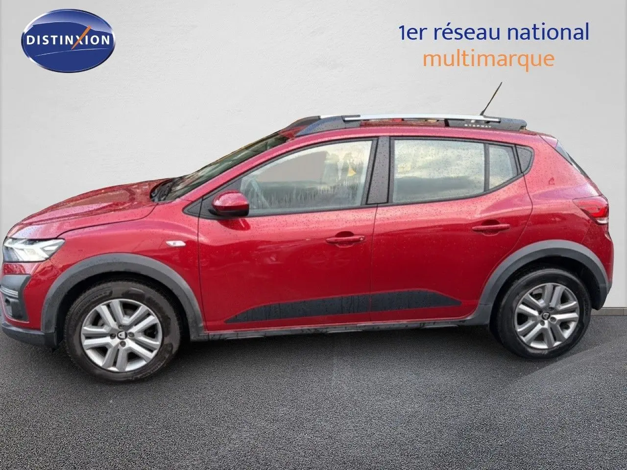 Vue de profil côté gauche d'une Dacia Sandero Stepway rouge fusion 2021 avec protections noires et jantes alliage.