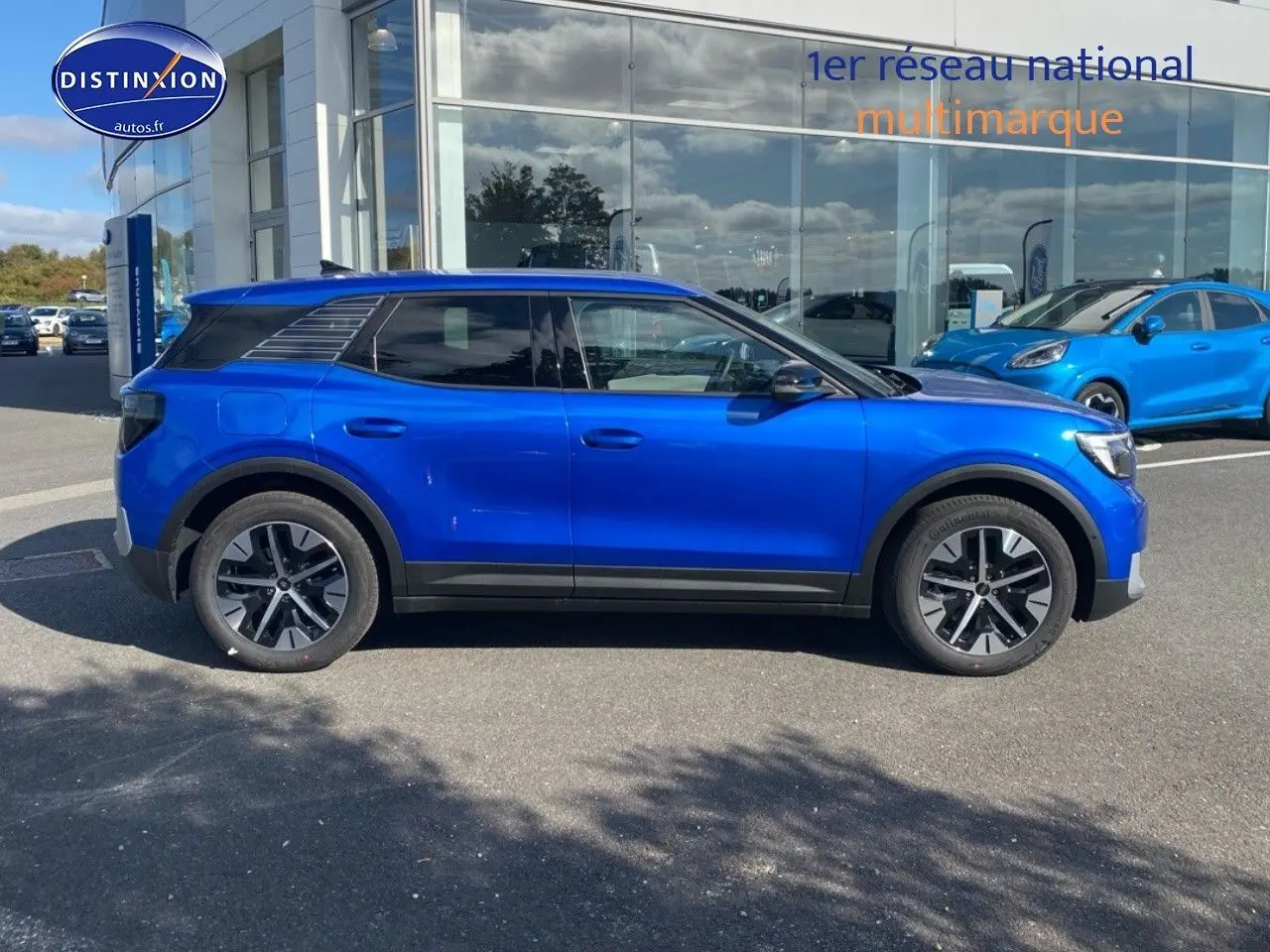 Ford Explorer électrique bleu Premium My Mind vu de profil côté gauche, stationné devant un bâtiment vitré.