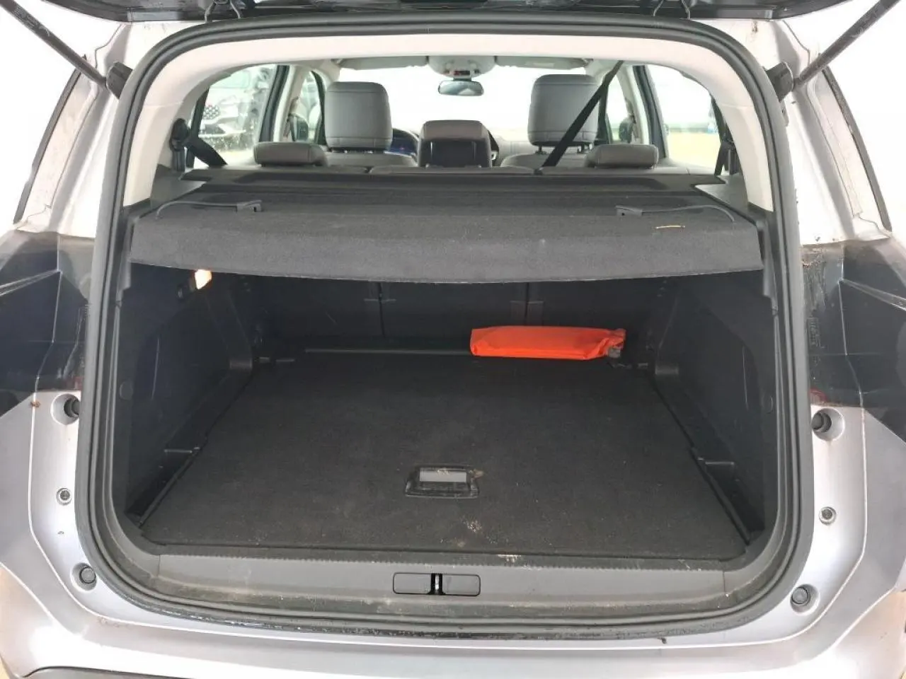 Coffre ouvert vu de l'arrière d'un Citroën C5 Aircross gris Artense avec cache-bagages et trousse de secours orange.