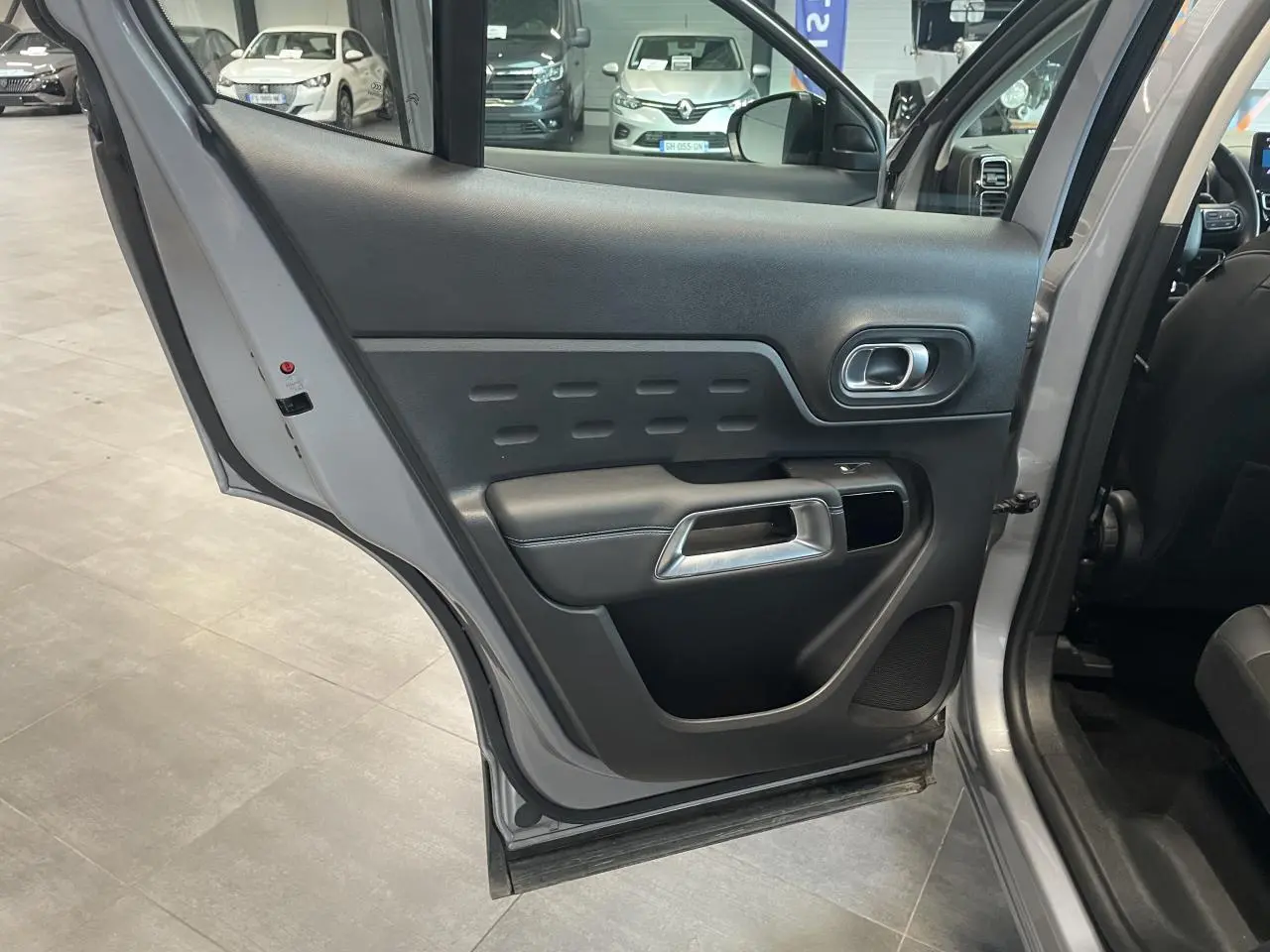 Vue rapprochée de la porte arrière droite ouverte du Citroën C5 Aircross gris Artense, montrant la garniture intérieure noire.