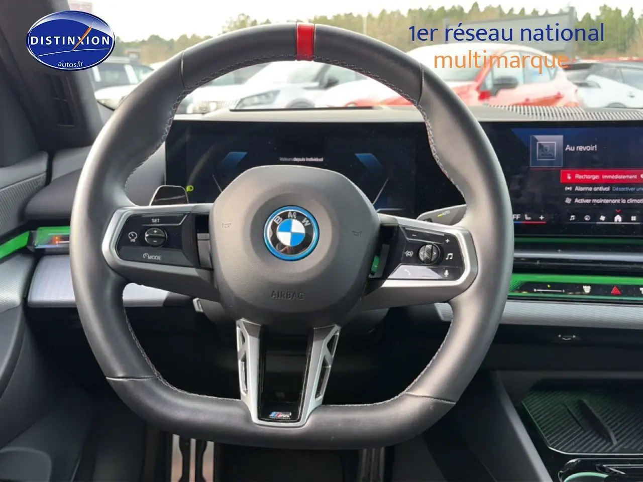 Vue intérieure centrée sur le volant sport noir avec bande rouge, tableau de bord digital et inserts verts de la BMW Série 5 i5 M60 2024.