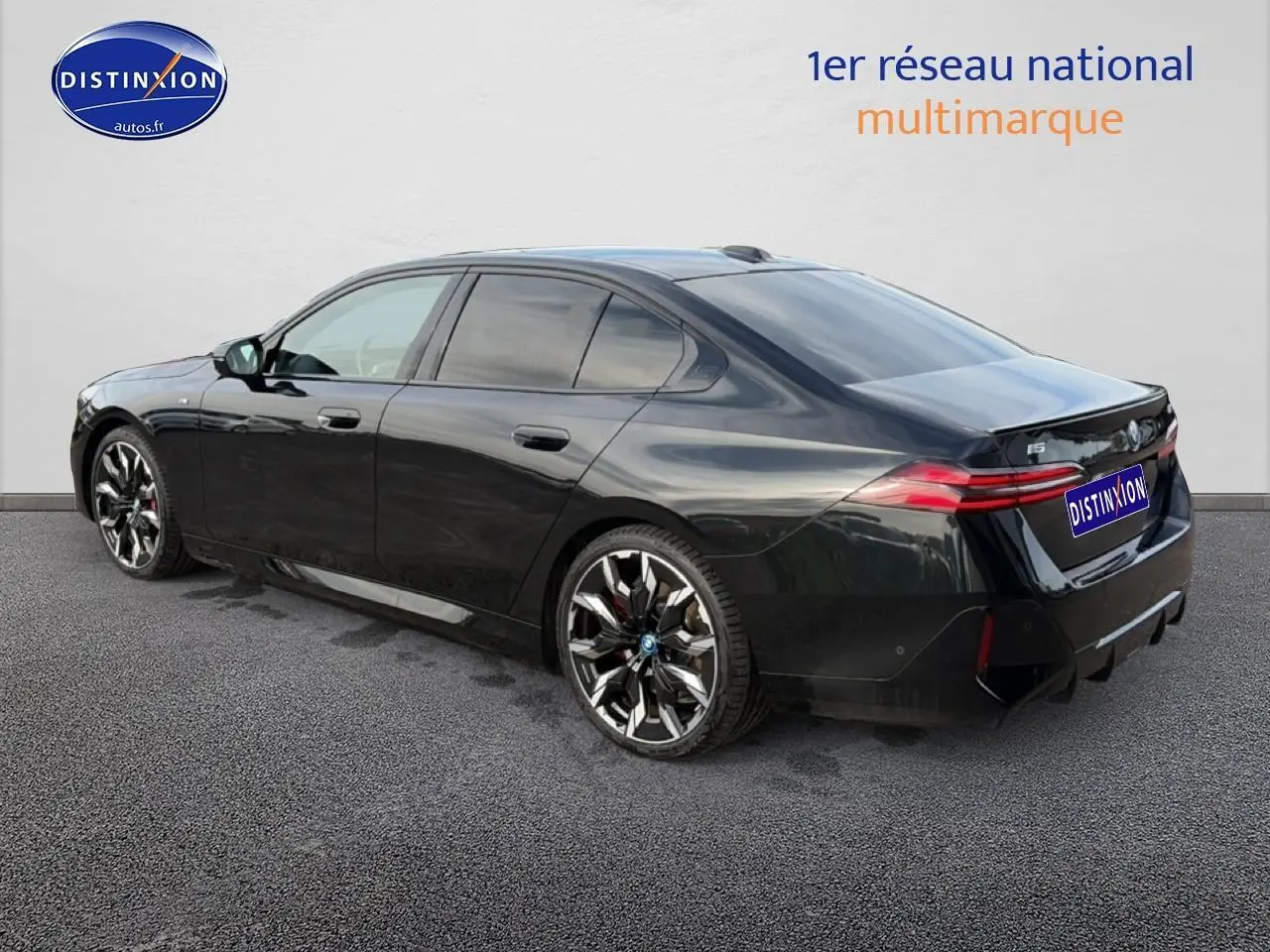 BMW Série 5 i5 M60 noir vue 3/4 arrière droit avec jantes alu bicolores et feux arrière LED allumés.