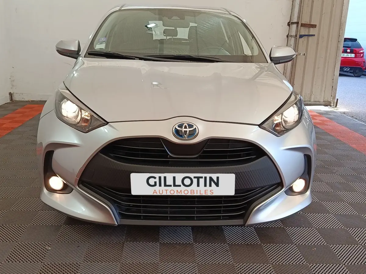 Vue frontale d'une Toyota Yaris hybride gris clair avec phares et antibrouillards allumés en intérieur.