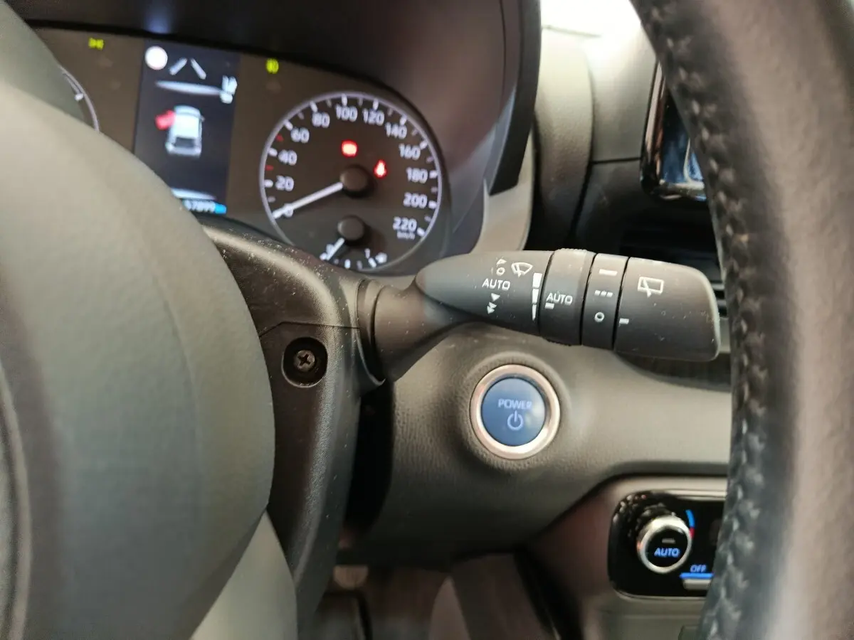 Vue rapprochée du tableau de bord de la Toyota Yaris hybride, avec bouton Power bleu et commandes au volant cuir noir.