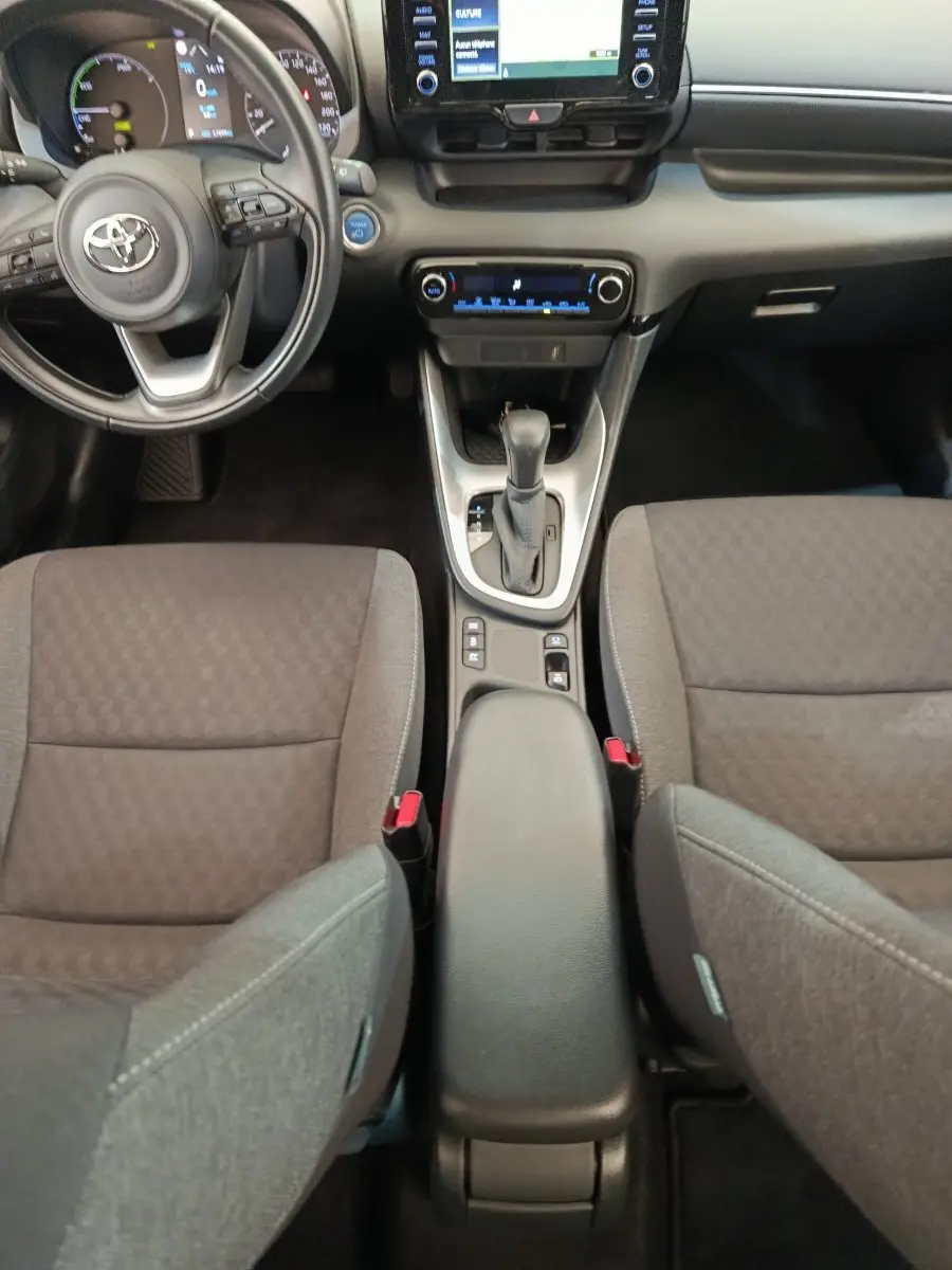 Vue intérieure de face centrée sur la console et volant cuir d'une Toyota Yaris hybride 2022, sièges gris foncé.