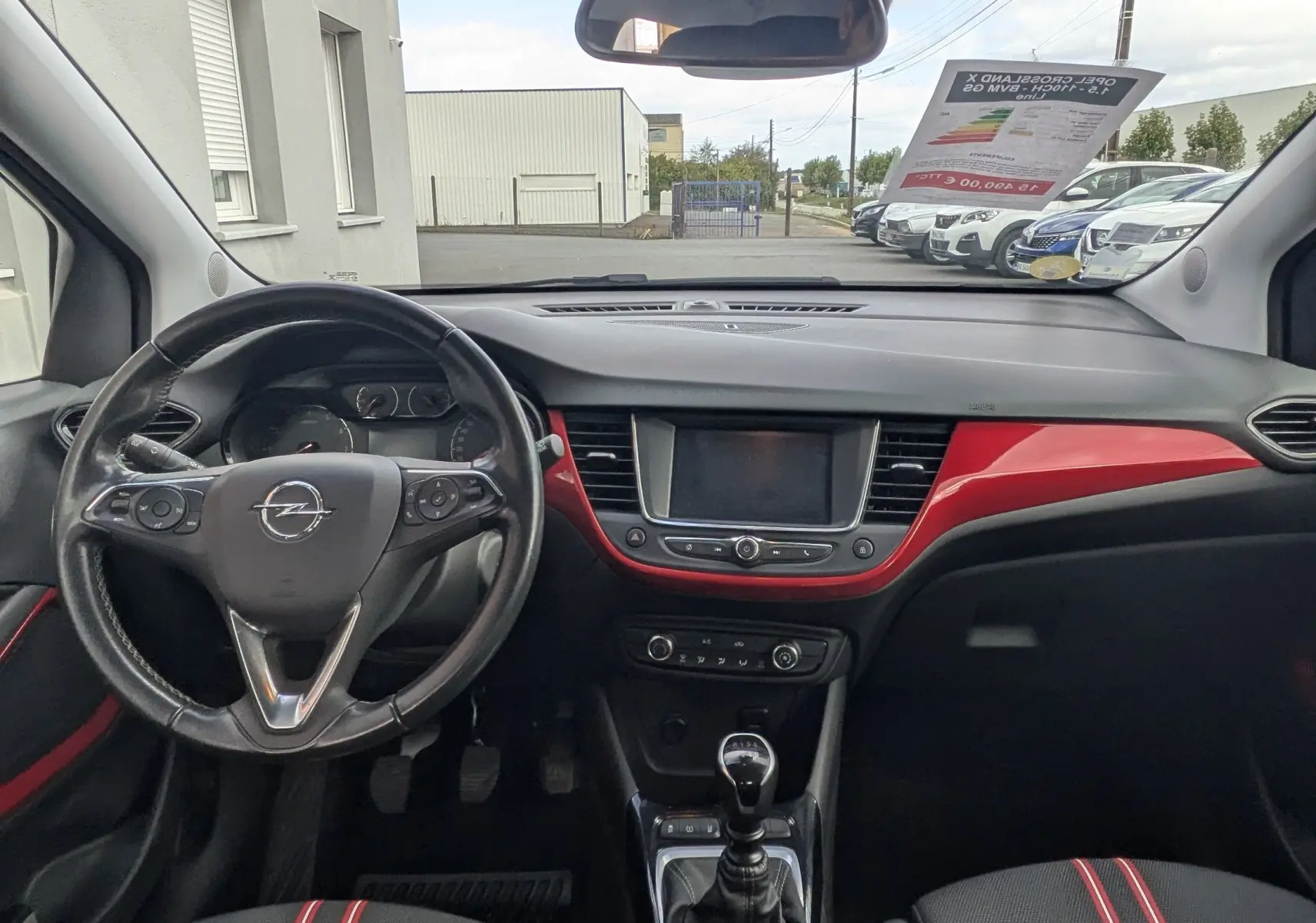 Vue intérieure avant de l'Opel Crossland X 2021, tableau de bord noir avec inserts rouges et sièges tissu noir à bandes rouges.