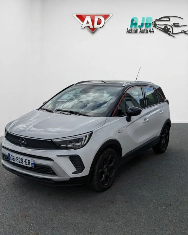 Opel Crossland X blanc en 3/4 avant droit avec toit noir et jantes noires, sur fond neutre intérieur.