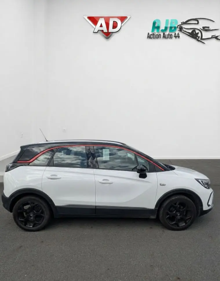 Vue de profil droit d'un Opel Crossland X blanc 2021 avec toit noir et jantes noires, souligné d'un liseré rouge.