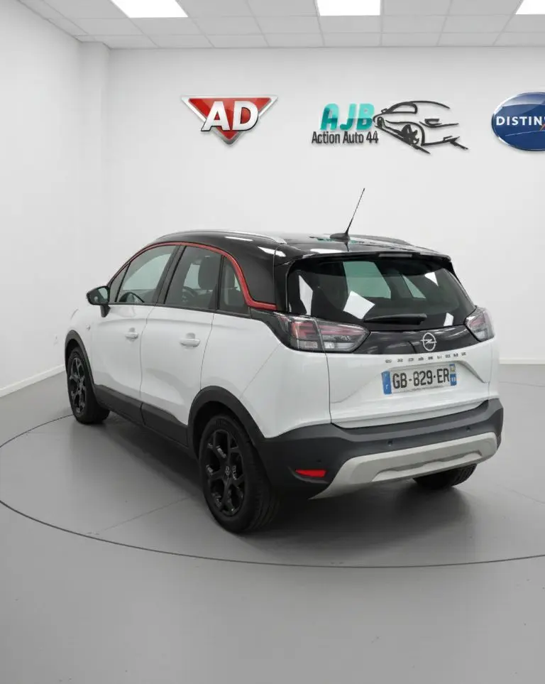 Vue 3/4 arrière droite d'un Opel Crossland X blanc avec toit noir et jantes noires en intérieur studio.