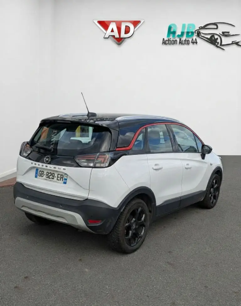 Opel Crossland X blanc 3/4 arrière droit avec toit noir, jantes noires et bandeau rouge autour des vitres.