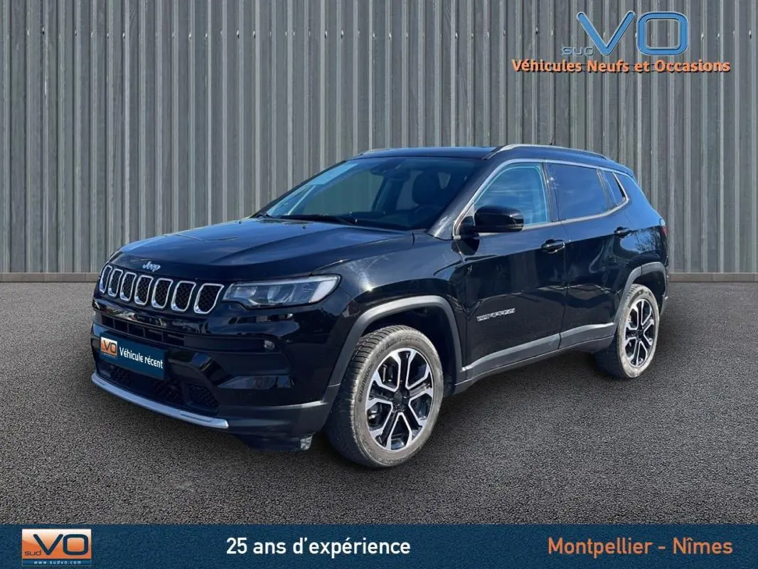 Jeep Compass noir vue 3/4 avant droit, avec barres de toit et jantes 18 pouces sur fond urbain.