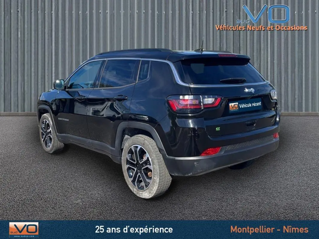 Vue 3/4 arrière droite d'un Jeep Compass noir 2023 avec barres de toit et jantes 18 pouces sur fond industriel.