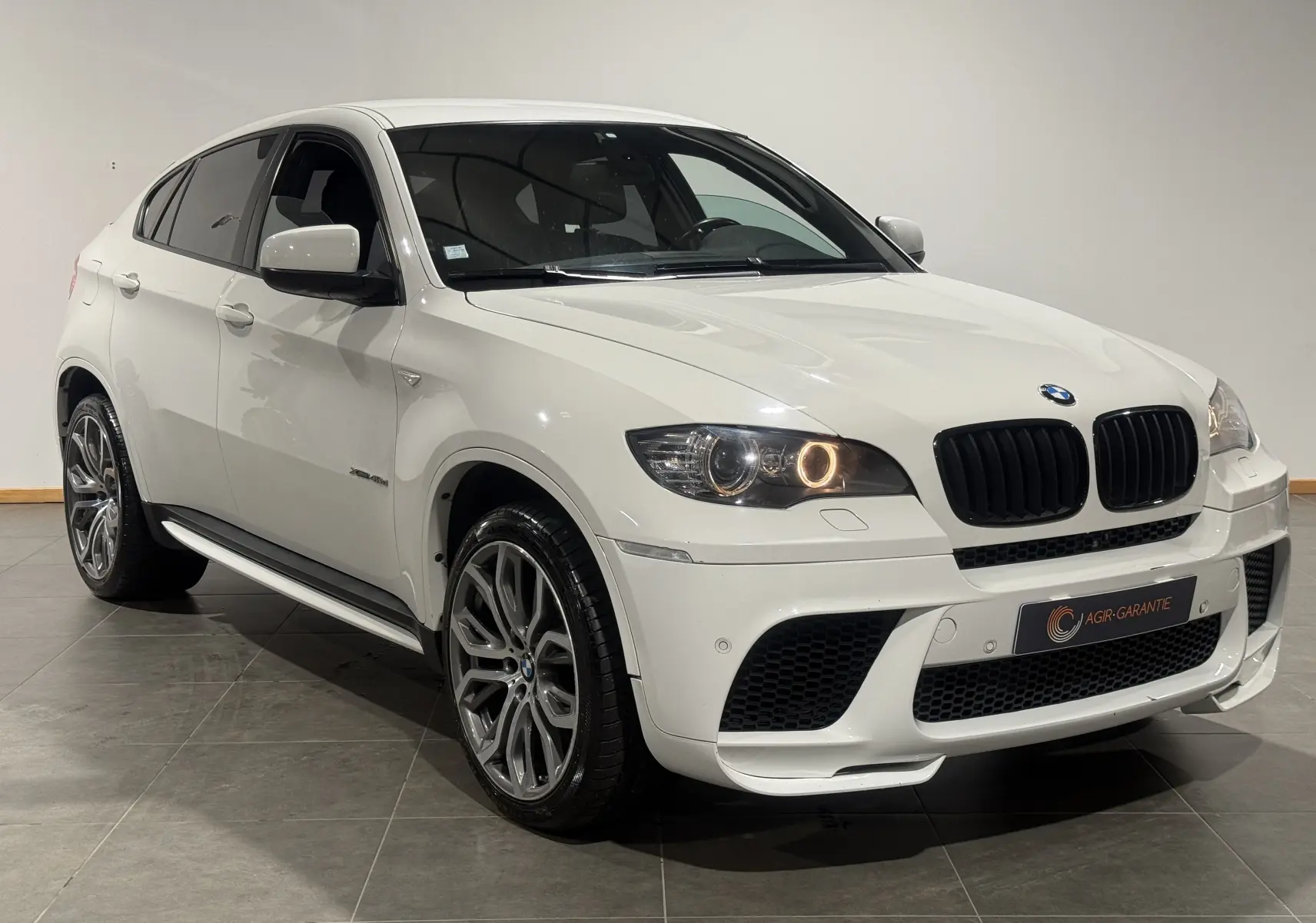 BMW X6 xDrive 40d blanc vue 3/4 avant droit, avec jantes M Sport et phares allumés en intérieur.