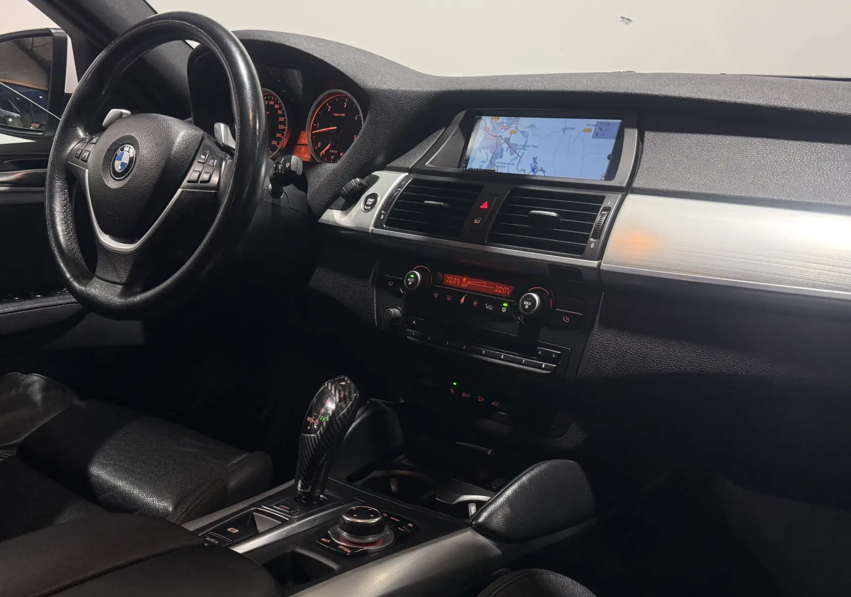 Vue intérieure côté conducteur du BMW X6 blanc 2026, mettant en valeur le tableau de bord avec écran de navigation et levier de vitesse M Sport.