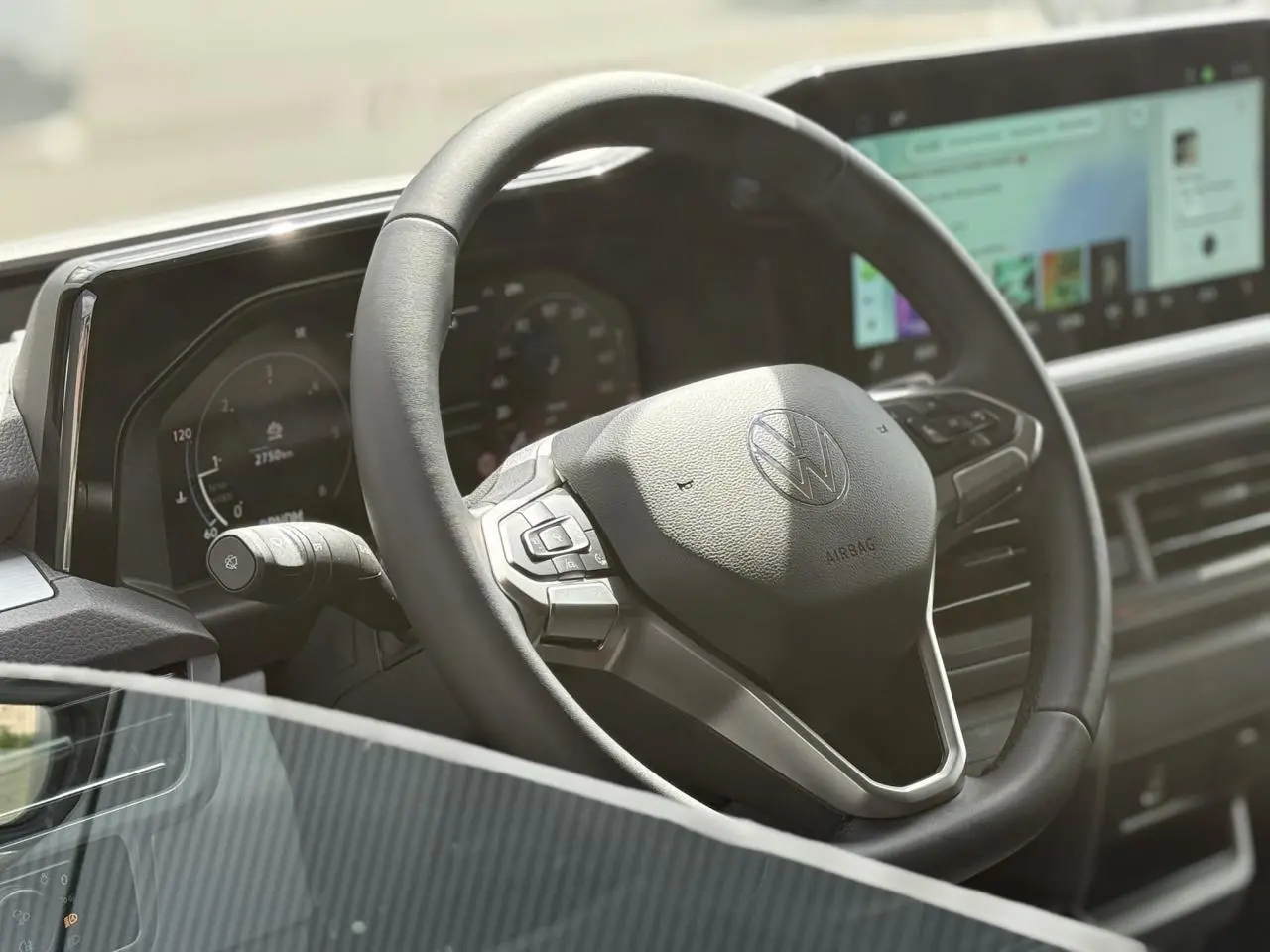 Gros plan sur le volant multifonction noir du Volkswagen Transporter T7 avec tableau de bord digital et écran tactile.